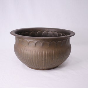 Peut inclure: Un grand pot rond en métal brun avec un bord festonné et des nervures verticales.