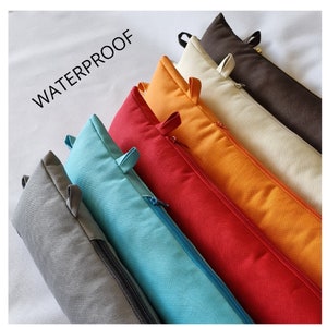 May include: A set of seven zippered cushion pads in various colours, including grey, blue, red, orange, beige, and brown. The cushions are arranged in a row and labelled "WATERPROOF".