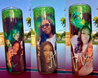 May include: A personalized tumbler with a green glitter top and a photo collage of three women. The tumbler has a black and green background with a butterfly design. The names "Amy" and "A" are written on the tumbler.