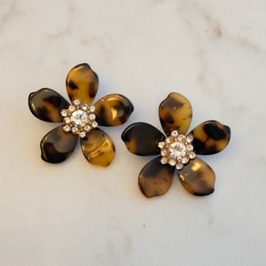 May include: A pair of tortoise shell flower-shaped earrings with clear rhinestone accents.