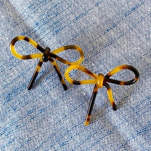 May include: Two brown and yellow tortoise shell hair clips shaped like bows.