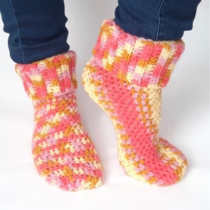 May include: A pair of crocheted slipper socks in pink, yellow, and orange. The socks have a striped pattern and are folded down at the top.