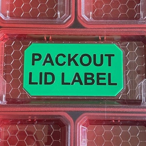 May include: A green label with the text "Packout Lid Label" on a red plastic storage container.