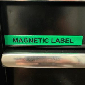 Könnte beinhalten: Ein grünes magnetisches Etikett mit dem Text "MAGNETIC LABEL" in schwarzer Schrift.