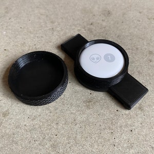 Op de afbeelding: Een zwarte plastic container met een deksel. Het deksel heeft een witte cirkel met een grijs alien gezicht en het nummer "1" erop.