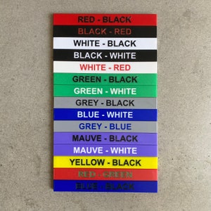 Op de afbeelding: Een set van 12 kleurgecodeerde labels met zwarte tekst. De labels lezen: Rood-Zwart, Zwart-Rood, Wit-Zwart, Zwart-Wit, Wit-Rood, Groen-Zwart, Groen-Wit, Grijs-Zwart, Blauw-Wit, Grijs-Blauw, Paars-Zwart, Paars-Wit, Geel-Zwart, Rood-Groen, Blauw-Zwart.