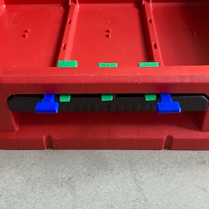 Op de afbeelding: Rode kunststof opbergdoos met een zwart deksel en groene en blauwe lipjes. De doos heeft drie compartimenten.