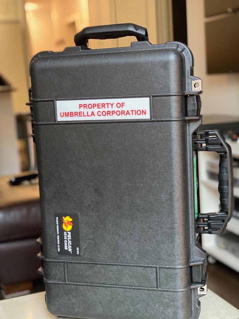 Op de afbeelding: Een zwarte Pelican 1610 koffer met een sticker waarop staat "PROPERTY OF UMBRELLA CORPORATION".