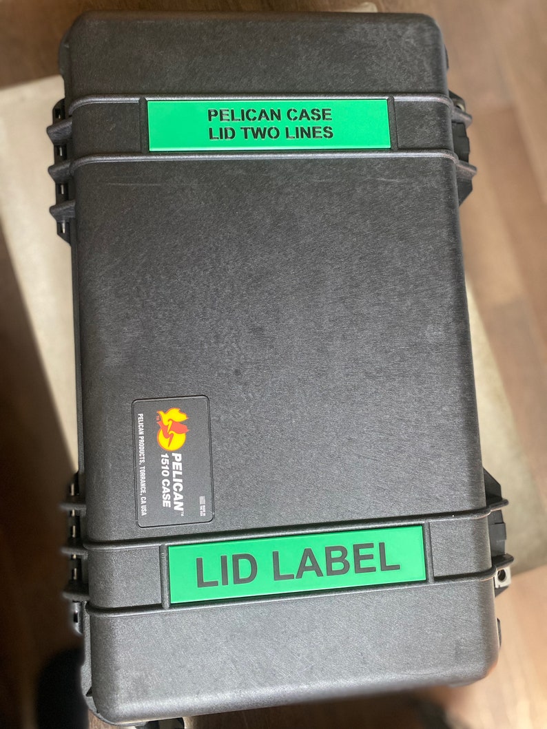 Pode incluir: Uma mala preta Pelican 1510 com etiquetas verdes que dizem "PELICAN CASE LID TWO LINES" e "LID LABEL". A mala tem um adesivo Pelican Products. A mala retangular tem um fecho de encaixe.