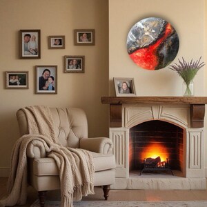 May include: A round, abstract painting with red, white, and black colors. The painting is hanging on a wall above a fireplace. The fireplace has a white mantel and a black fire grate.