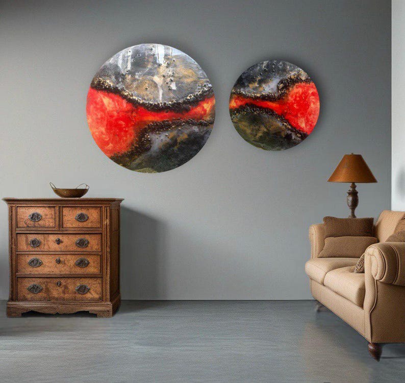 May include: Two round abstract paintings with a red, black, and gold color scheme. The paintings are hanging on a gray wall above a wooden dresser and a brown couch.