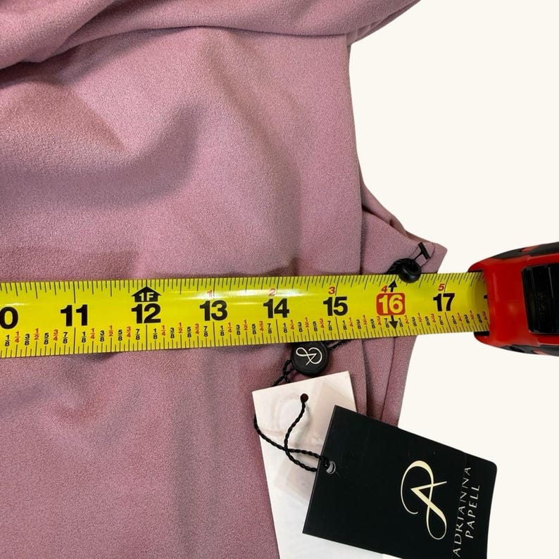 Puede incluir: Vestido rosa empolvado con una cinta m&eacute;trica que muestra una medida de 40,6 cm. El vestido tiene botones negros y una etiqueta de Adrianna Papell.