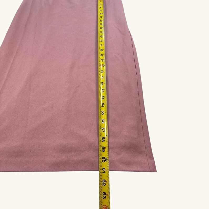 Puede incluir: Una prenda de color rosa polvoriento, posiblemente una falda o un vestido, se mide con una cinta m&eacute;trica amarilla. La cinta muestra medidas de hasta 160 cm. La tela parece ser de color liso y tiene una textura suave.
