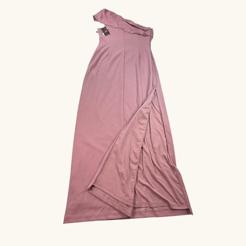 Puede incluir: Vestido largo asim&eacute;trico rosa empolvado con una abertura alta. El vestido presenta un escote drapeado y un corpi&ntilde;o entallado. Una etiqueta est&aacute; adjunta. El vestido est&aacute; hecho de una tela suave y fluida.