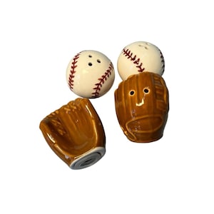 Puede incluir: Un juego de salero y pimentero con temática de béisbol. El juego incluye dos saleros con forma de pelota de béisbol con costuras rojas y dos saleros con forma de guante de color marrón. Los saleros de béisbol tienen tres agujeros en la parte superior.