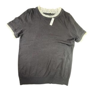 May include: A dark gray short-sleeve sweater with a cream-colored lace trim around the neckline and sleeve cuffs. A white tag is attached to the neckline. The sweater has a ribbed hem.