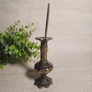 May include: An antique brass incense holder, featuring a long, thin pin. The holder has an intricate design, with a star-shaped base and a rounded body. The brass has a warm, aged patina, indicating its vintage origins.