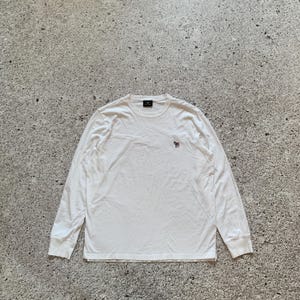 May include: A white long-sleeve shirt with a crew neck and a small embroidered zebra logo on the chest. The shirt is made of a soft material and has ribbed cuffs.