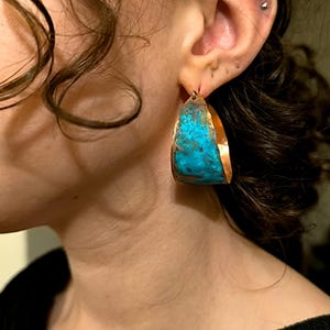 May include: A pair of large, copper hoop earrings with a turquoise patina finish. The earrings are handmade and have a unique, organic shape.
