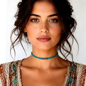 Puede incluir: Primer plano de una persona que lleva un collar gargantilla de cuentas turquesas. El collar es de un color azul verdoso vibrante y se coloca cerca del cuello. La persona lleva una blusa estampada con tonos tierra.