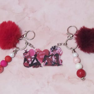 May include: Two keychains with silver rings, red pom-poms, and beaded accents. One keychain has a red, pink, and white bead strand, while the other has a white, pink, and red bead strand. Both have a heart-shaped charm with the text "F*** ME".