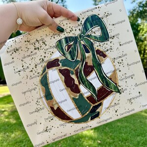 May include: A square canvas with a painted design featuring a green bow and a sphere with a camouflage pattern in green, brown, and white. The text "PNG | SVG | DXF" is at the bottom.