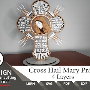 May include: A four-layer laser-cut wooden cross featuring a central illustration of Mary in a brown head covering. The cross is inscribed with the Hail Mary prayer in white text against a dark background, accented with white starburst points.