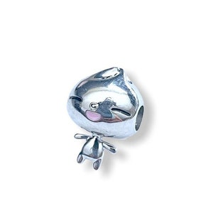 May include: Silver charm with a cartoon character design. The character has a round head with a pink face and a small body with arms and legs.