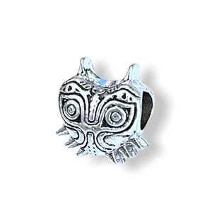 May include: A silver charm featuring a detailed Majora's Mask design from the Legend of Zelda video game series.