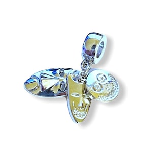 May include: Silver charm with three dangling charms: a mask, a skull, and a round charm with a face. The charms are attached to a silver bead.