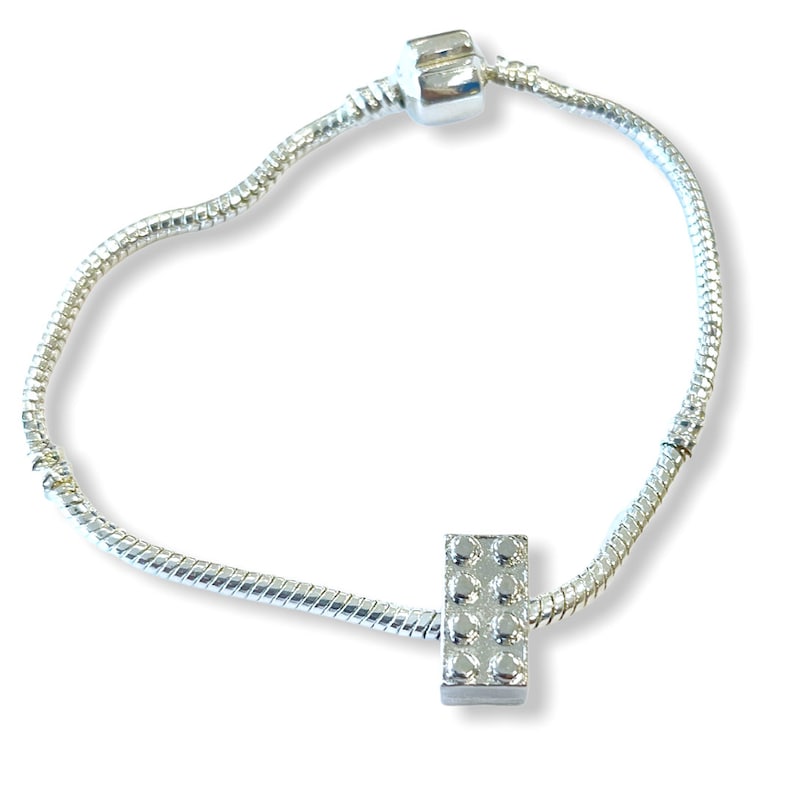 May include: A silver charm bracelet with a silver charm shaped like a Lego brick.