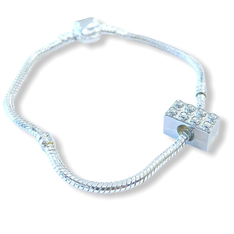 May include: A silver snake chain bracelet with a silver charm featuring a rectangular design with clear rhinestones.