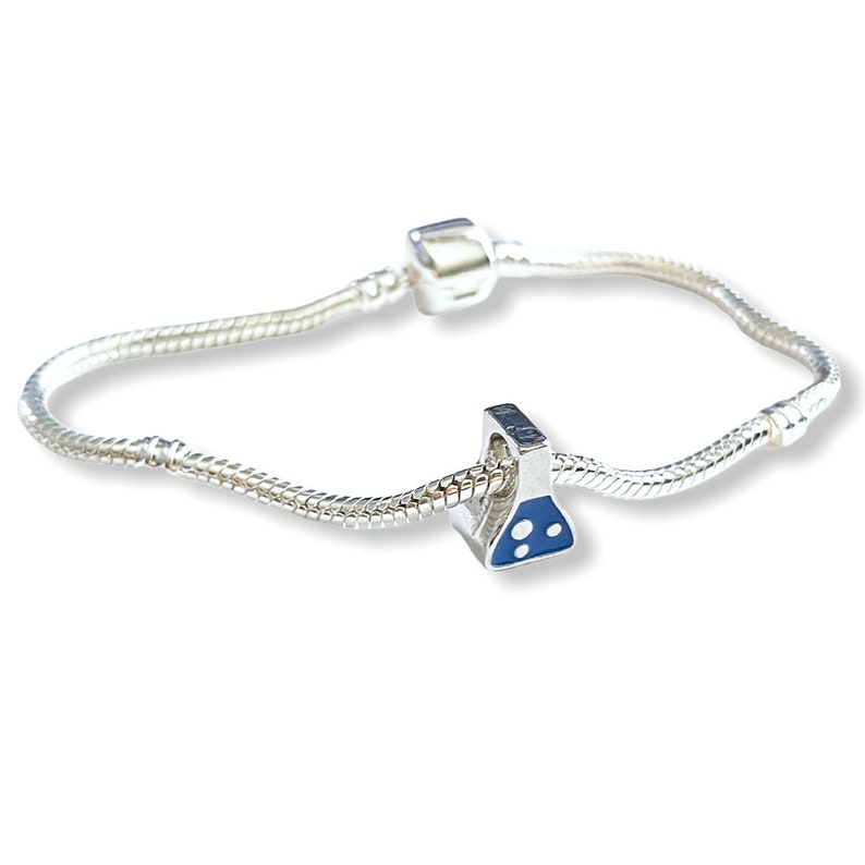 May include: A silver charm bracelet with a science beaker charm. The charm is silver with a blue enamel design. The bracelet is made of a silver snake chain with a barrel clasp.