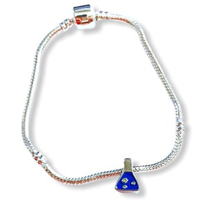 May include: A silver-colored charm bracelet with a science-themed charm. The charm is a blue and silver flask with three white bubbles. The bracelet has a snake chain design and a barrel clasp.