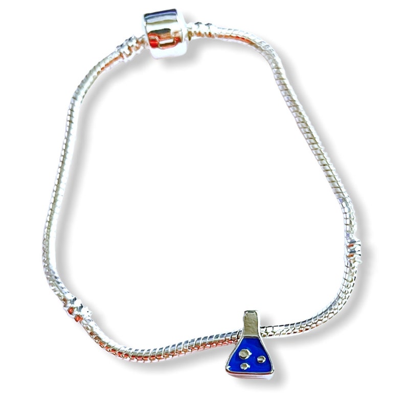 May include: A silver-colored charm bracelet with a science-themed charm. The charm is a blue and silver flask with three white bubbles. The bracelet has a snake chain design and a barrel clasp.