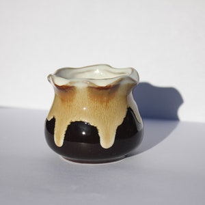 May include: A small, brown and white ceramic pot with a wavy rim. The pot has a glazed finish and a drip glaze design.