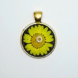 May include: A gold pendant with a yellow flower pressed inside a clear resin circle.