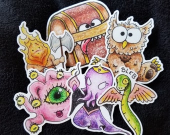 May include: A set of colorful cartoon stickers featuring a treasure chest, an owl, a fire creature, a purple octopus, a green snake with wings, and a pink creature with three eyes. The stickers are all hand-drawn and have a whimsical style.