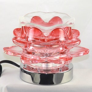 Puede incluir: Un difusor de aceite de vidrio rosa con forma de flor de loto con una base plateada y un cable.