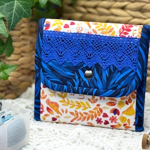 May include: A small blue and white fabric pouch with a blue lace trim and a button closure. The pouch has a floral pattern with birds and leaves.