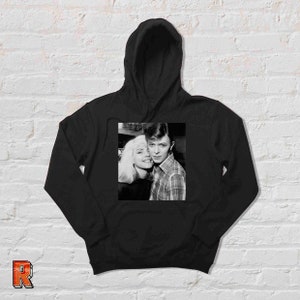 May include: Black and white photo of David Bowie and a woman with blonde hair. The photo is printed on a black hoodie.