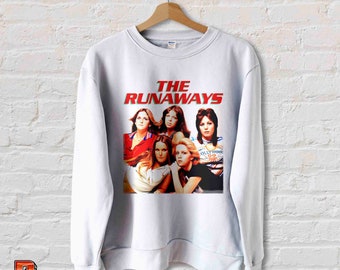 May include: White sweatshirt with a vintage-style graphic print of the band "The Runaways" featuring five women in a band pose. The text is in red.