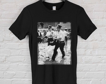 May include: Black and white photo print of a man being arrested by a police officer. The photo is printed on a black t-shirt.