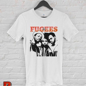 May include: White t-shirt with a black and white image of the hip-hop group The Fugees. The band's name is printed in red letters above the image.