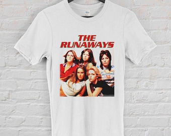 May include: White t-shirt with a graphic of the band The Runaways. The graphic features a photo of the band members in a group pose. The band's name is written in red letters above the photo.
