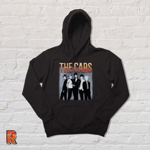 May include: Black hooded sweatshirt with a vintage-style graphic of the band "The Cars" in orange and yellow text. The band members are pictured in black and white.