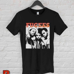 May include: Black t-shirt with a white graphic of the hip-hop group The Fugees. The group members are shown in black and white, with the band name in red and orange.