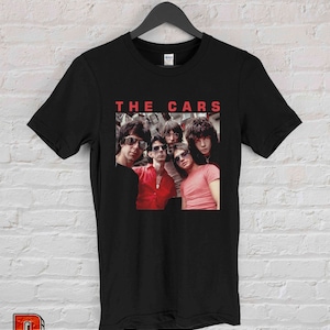 May include: Black t-shirt with a red graphic of the band The Cars. The graphic features a photo of the band members in black and white, wearing sunglasses and red shirts.