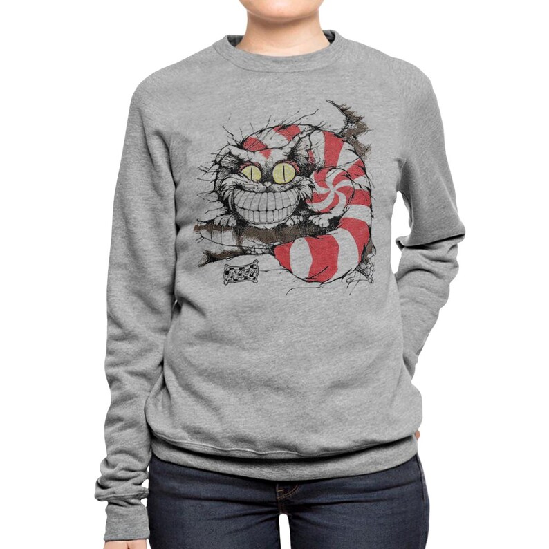 May include: A gray sweatshirt featuring a grinning Cheshire Cat illustration. The cat has a red and white striped tail and a large, toothy smile. The graphic is a whimsical design, perfect for fans of fantasy and literature.