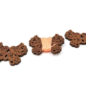 May include: Three wooden butterfly-shaped thread holders. One holder has a spool of peach-colored thread.